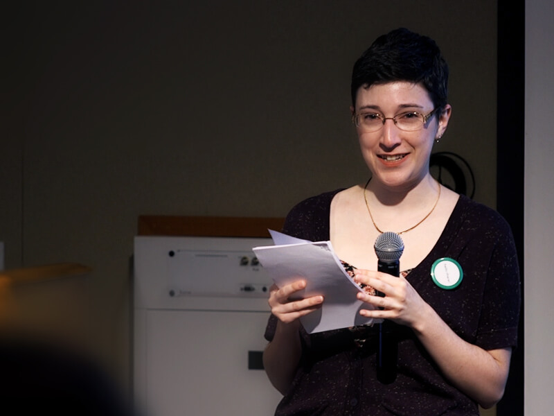 Photo of Diane Murray smiling and holding a mic and notes