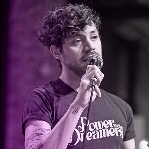 Photo of Helday de la Cruz wearing a "Power to the Dreamers" shirt and speaking into a microphone