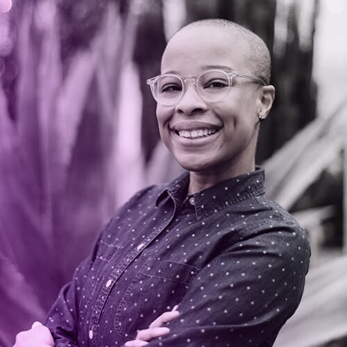 Photo of Neesha Powell-Twagirumukiza smiling and facing the camera while standing slightly angled with crossed arms