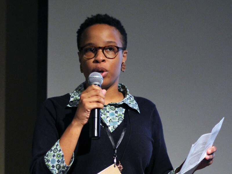 Neesha Powell-Twagirumukiza speaking into mic while holding notes